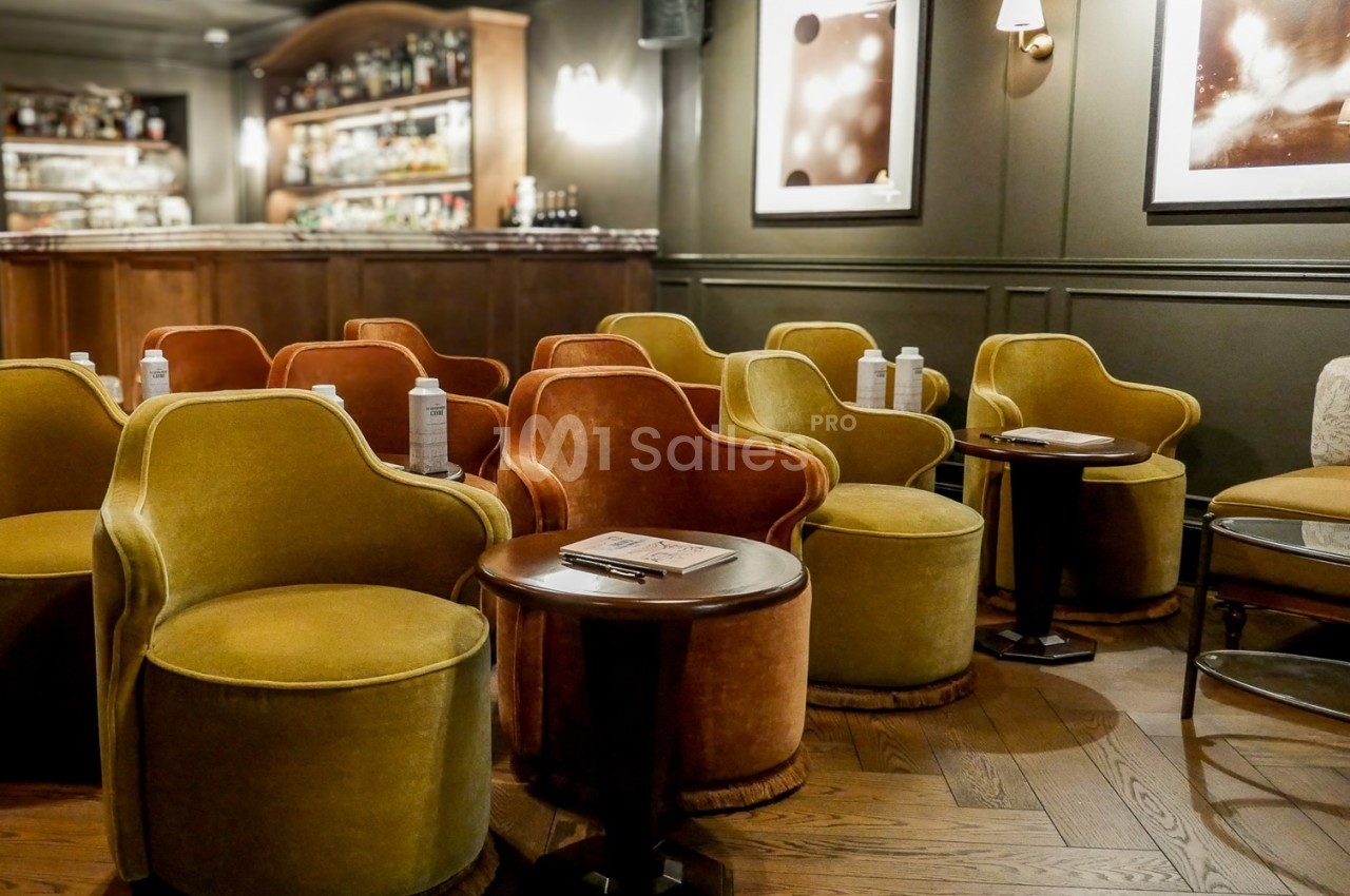 Fauteuils colorés disposés autour de petites tables dans un bar élégant avec un comptoir en bois en arrière-plan.