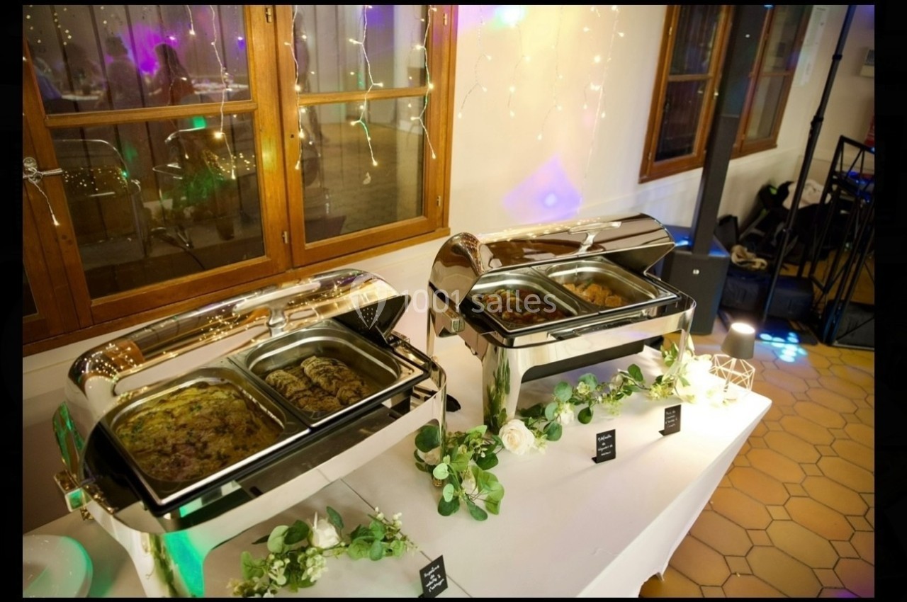 Buffet chaud avec plats variés présentés dans des chafing dishes en inox, décoré de fleurs et guirlandes lumineuses.