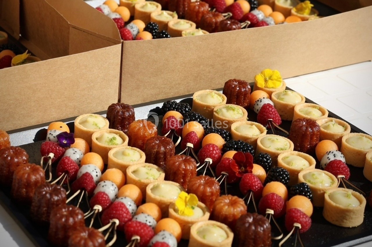 Plateau de mignardises variées comprenant cannelés, tartelettes, fruits frais et brochettes colorées.