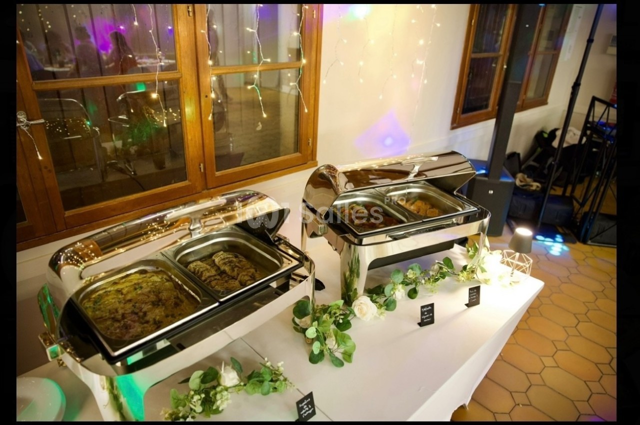 Buffet chaud avec plats variés présentés dans des chafing dishes en inox, décoré de guirlandes et de fleurs.