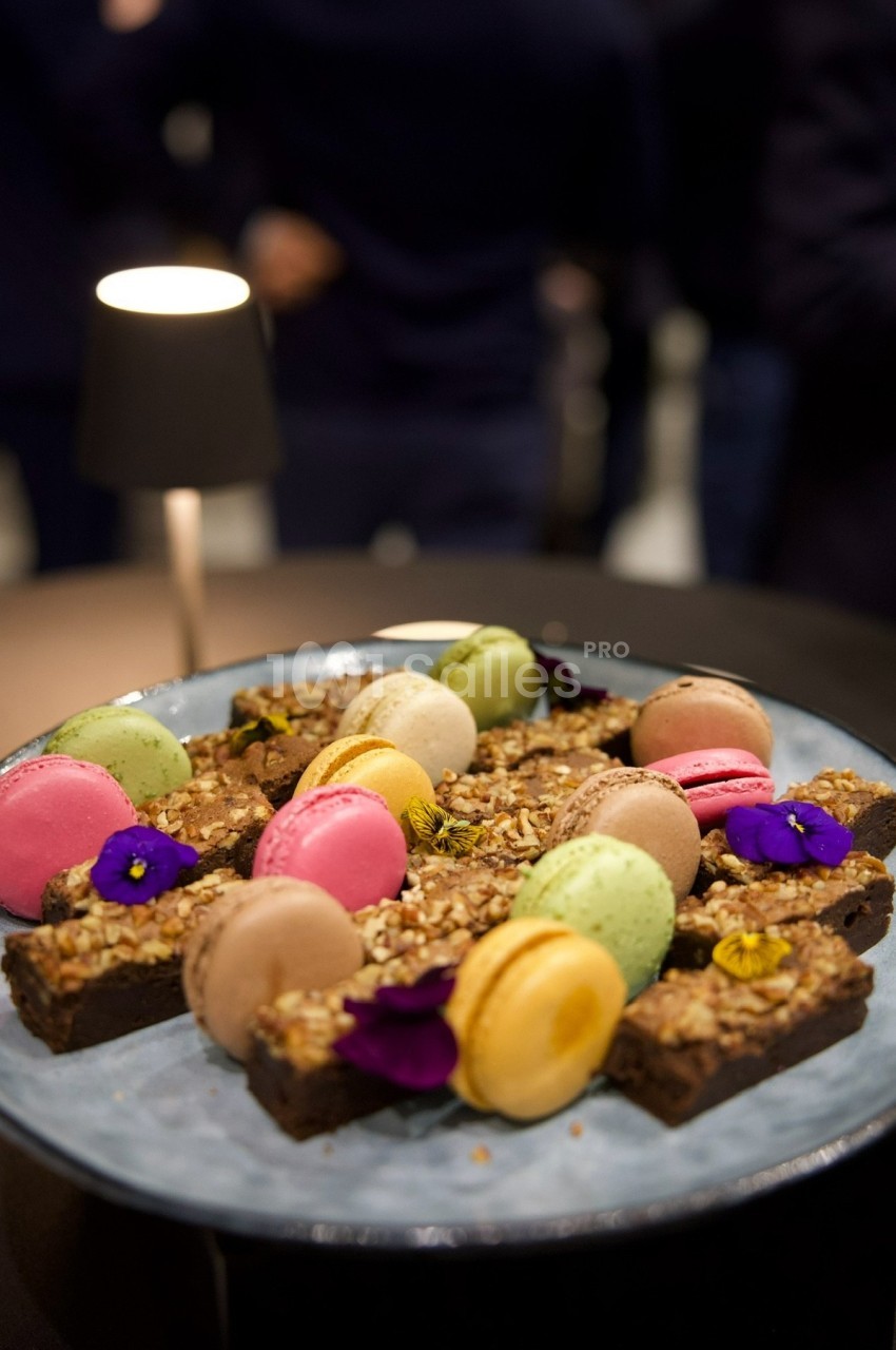 Assortiment de macarons colorés et brownies garnis de noix, présenté sur une assiette sous une lumière tamisée.