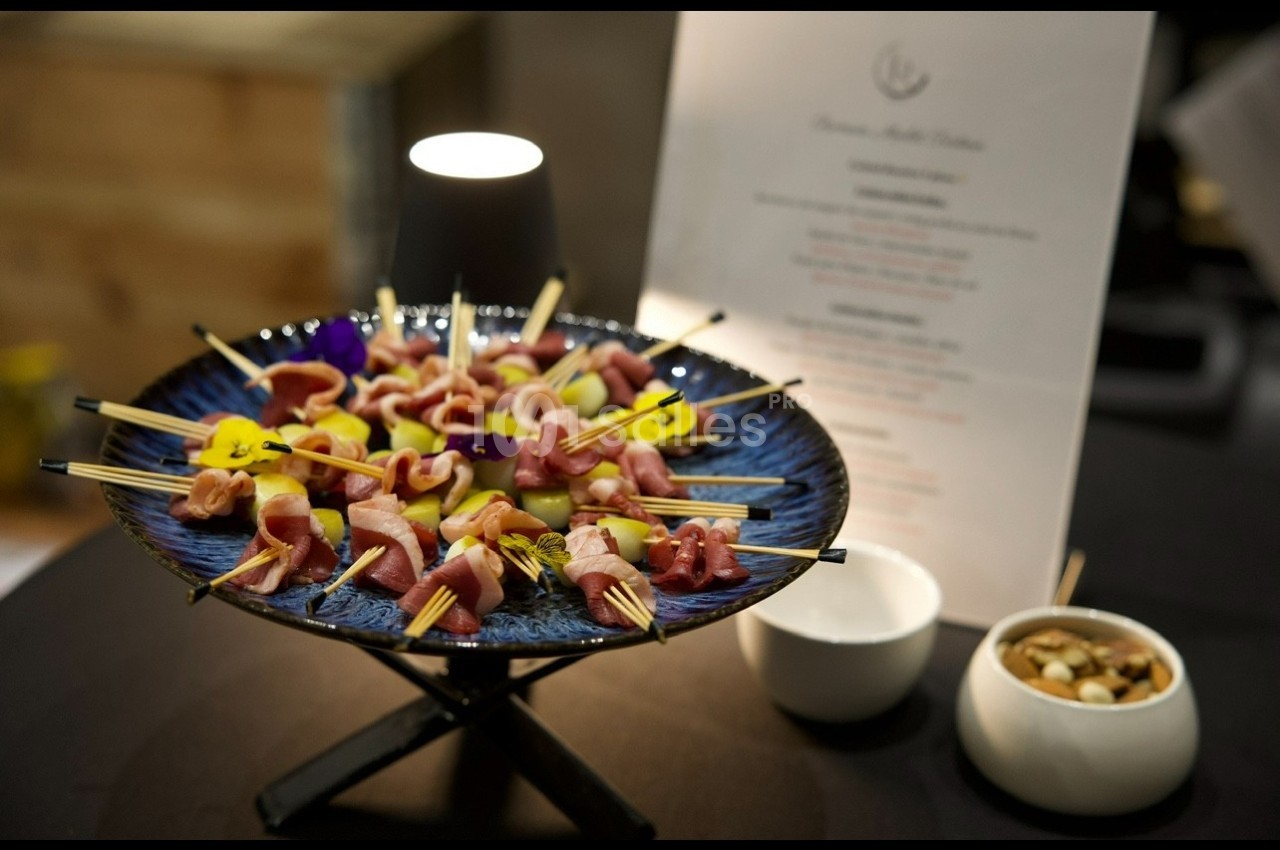 Assortiment de brochettes apéritives sur un plateau bleu, accompagné de bols et d'une carte de menu en arrière-plan.
