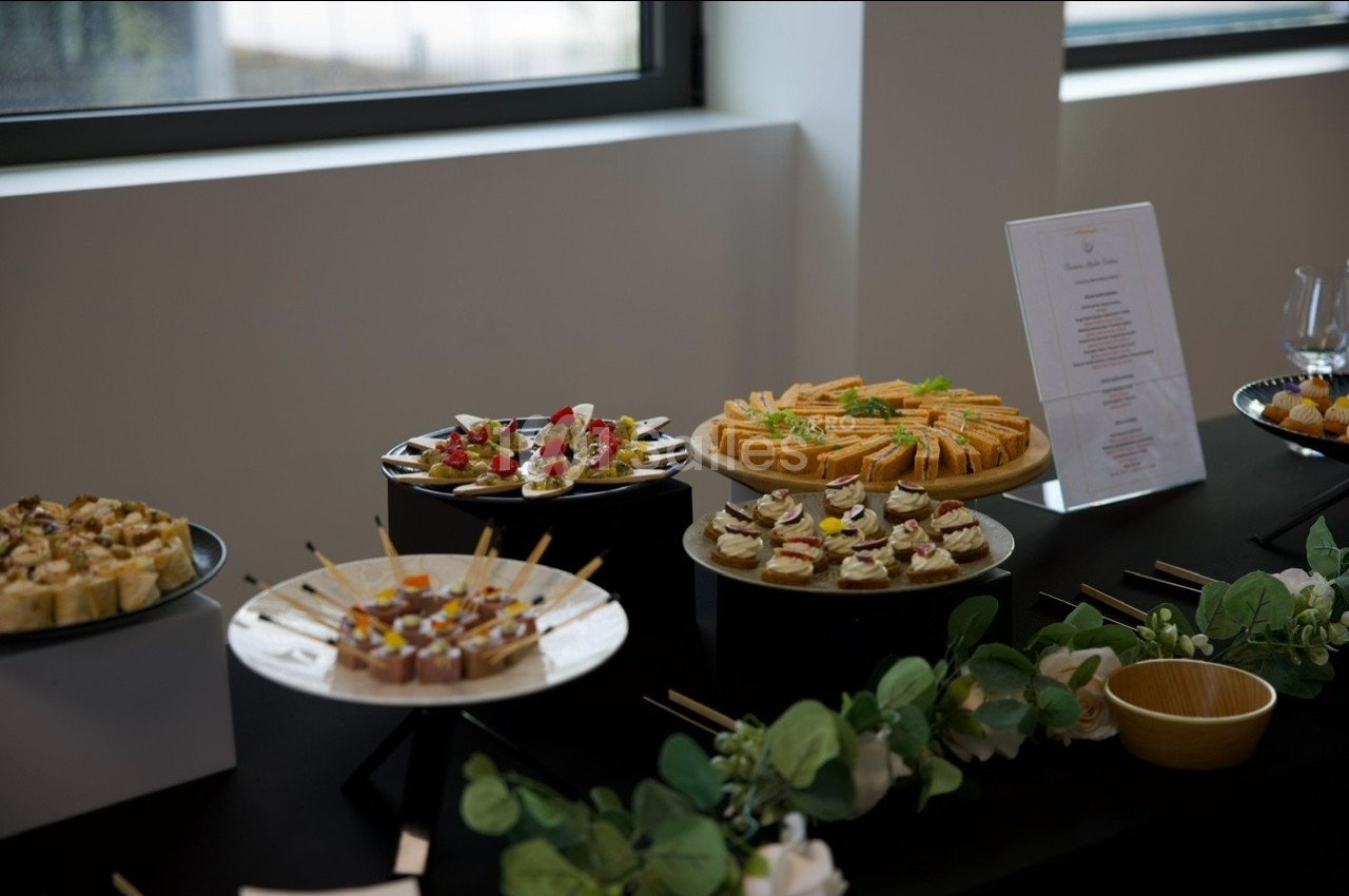 Buffet de canapés variés disposés sur des plateaux noirs, décoré de verdure, près d'une fenêtre.