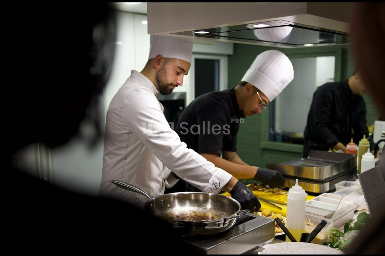 Deux chefs cuisiniers en tenue blanche préparent des plats dans une cuisine professionnelle.