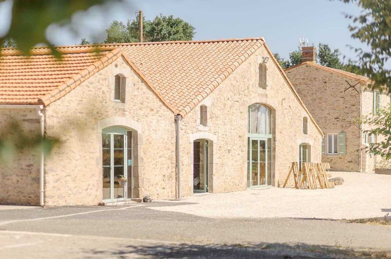Bâtiment en pierre avec toit en tuiles rouges, grandes baies vitrées et espace extérieur ensoleillé.
