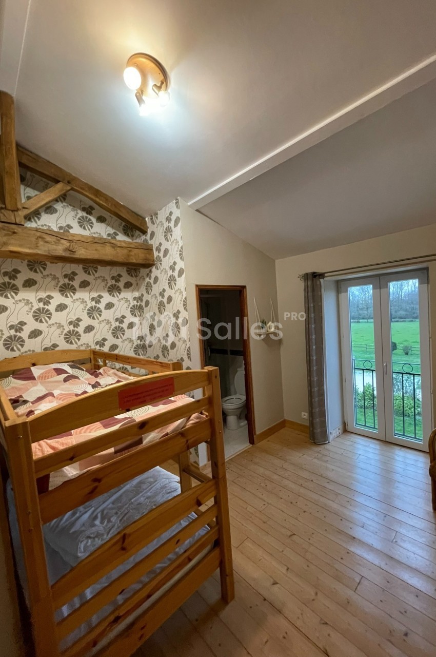 Chambre avec lits superposés en bois, parquet, papier peint floral, porte-fenêtre donnant sur un jardin.