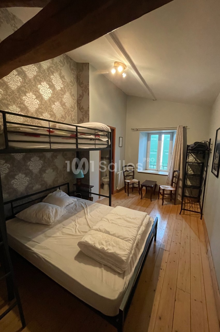 Chambre avec lit superposé, lit double, parquet en bois, fenêtre lumineuse et mobilier simple.