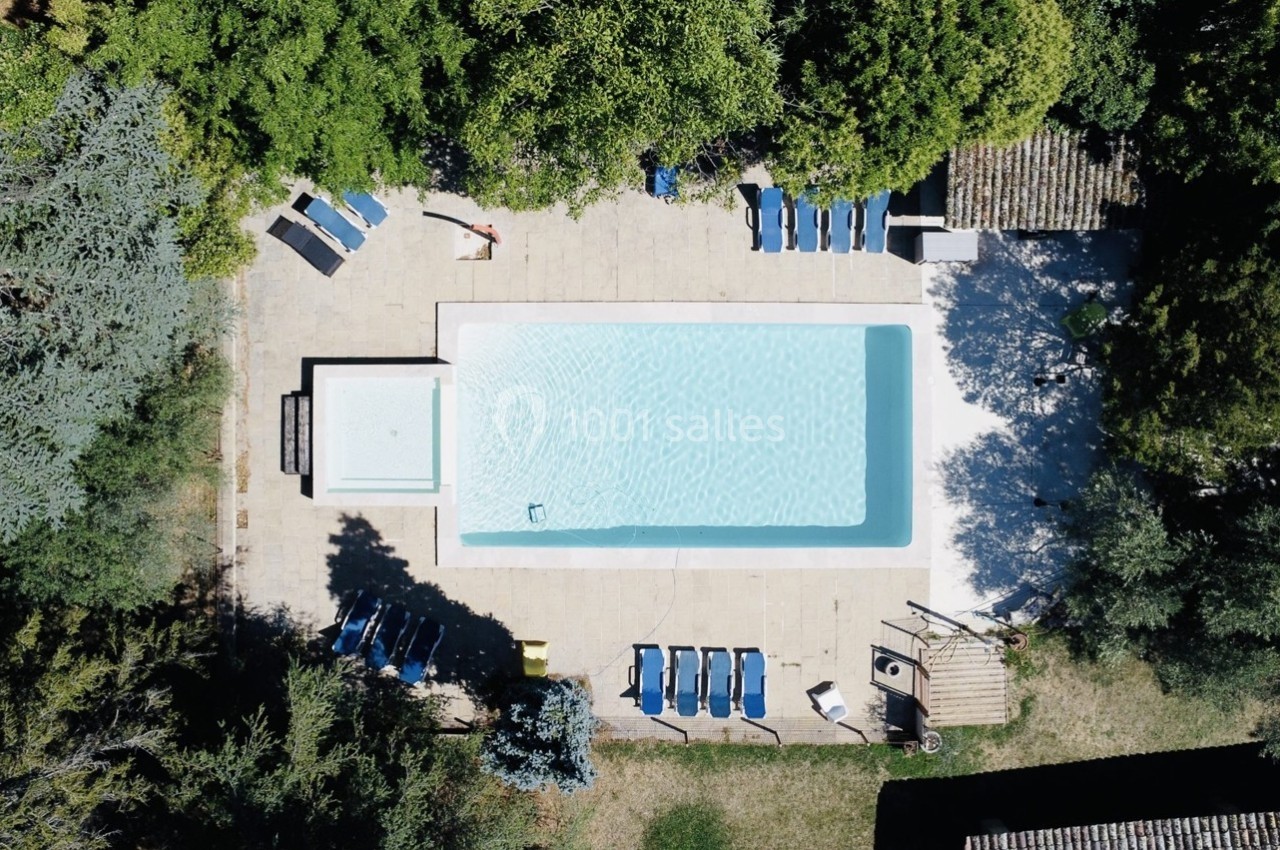 Vue aérienne d'une piscine extérieure entourée de chaises longues, de végétation et de bâtiments en pierre.