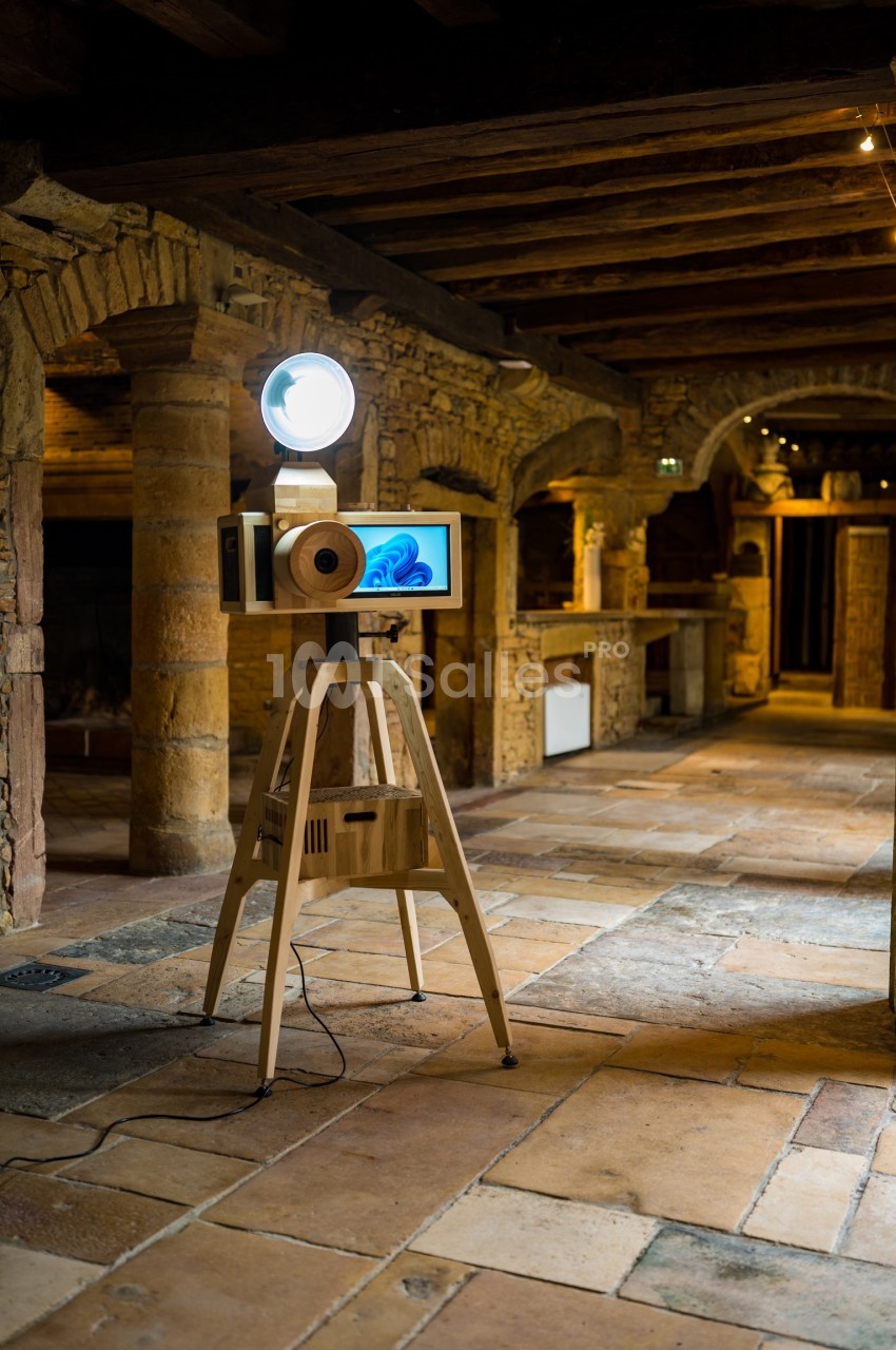 Installation artistique en bois avec écran et projecteur, située dans un espace intérieur aux murs en pierre et poutres…
