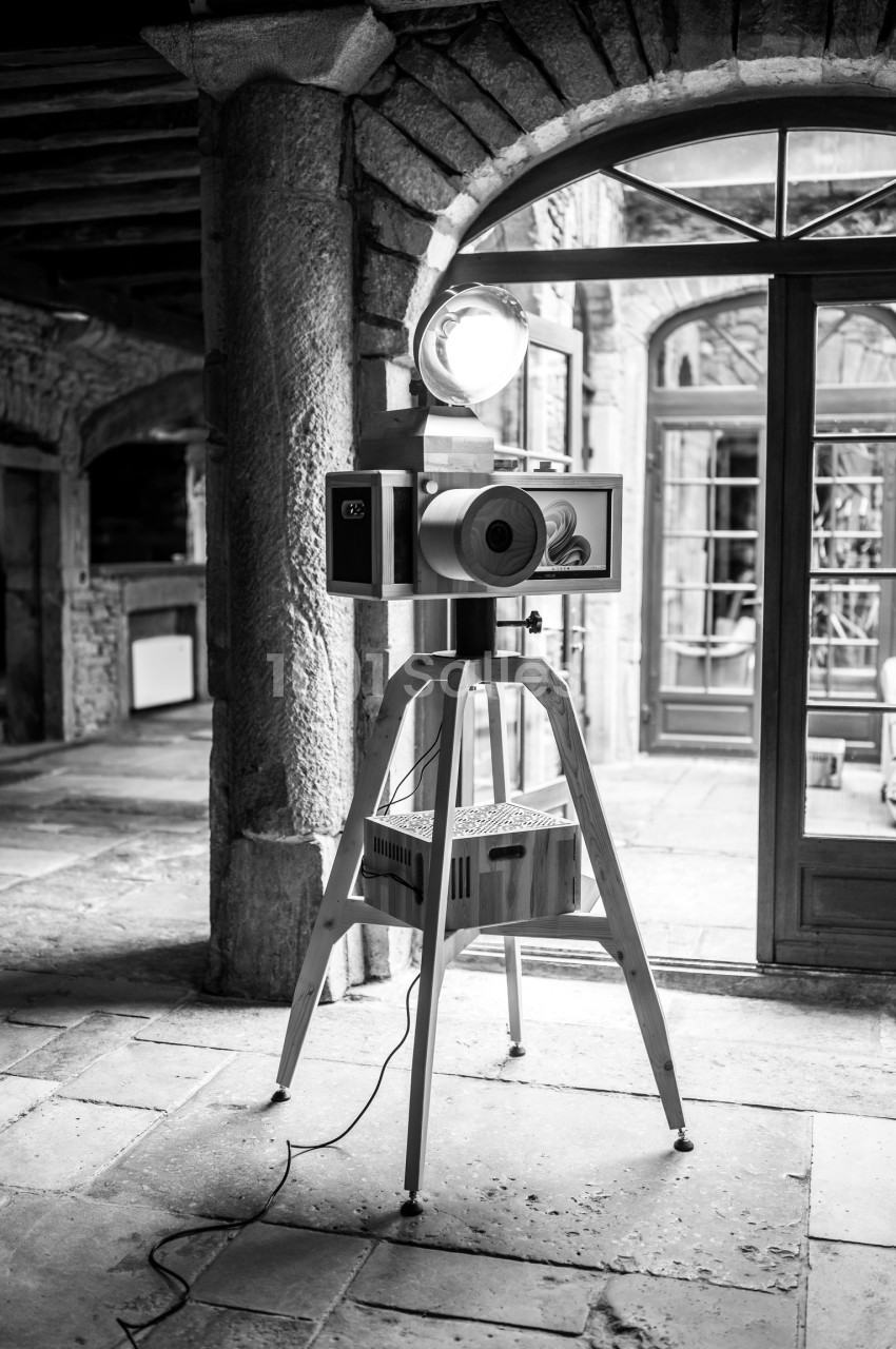 Projecteur vintage sur trépied en bois dans un intérieur en pierre avec des arches et des portes vitrées.