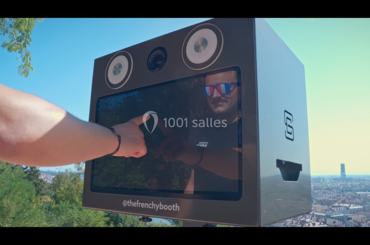 Une personne interagit avec un photobooth moderne en extérieur, avec une vue urbaine en arrière-plan.