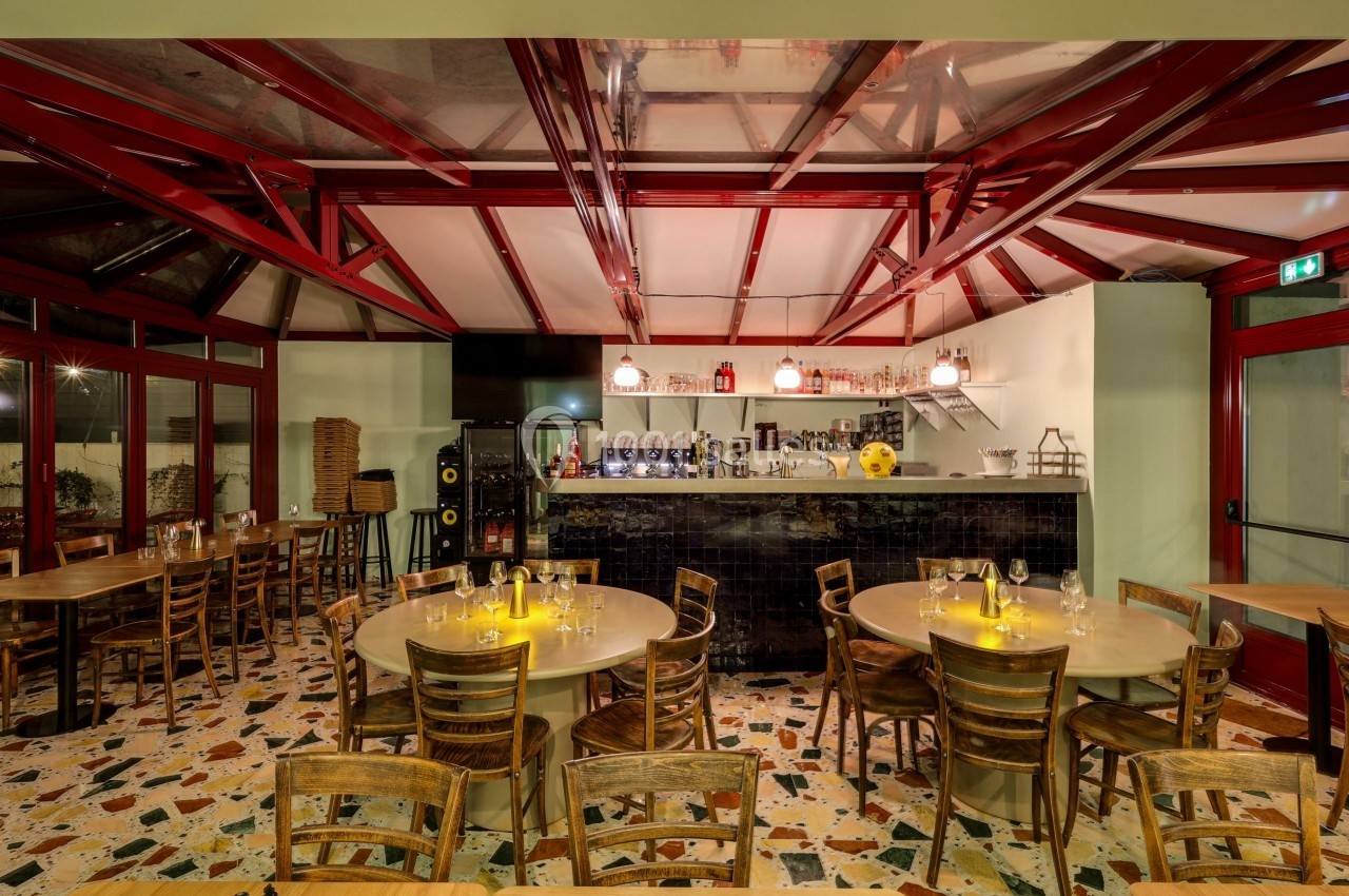 Salle de restaurant avec tables en bois, chaises assorties, éclairage chaleureux et comptoir de bar en arrière-plan.