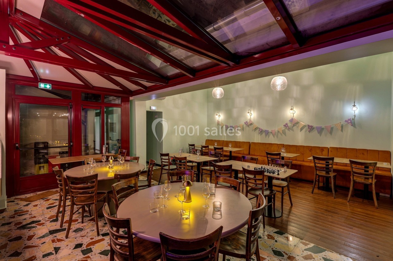 Salle de restaurant avec tables rondes dressées, éclairage chaleureux et guirlandes décoratives sur un mur clair.