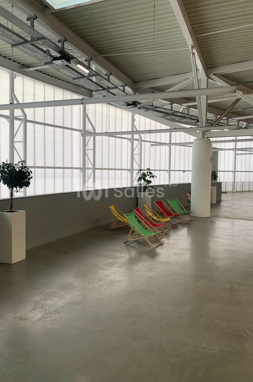 Chaises longues colorées alignées dans un espace intérieur lumineux avec des plantes en pot et un sol en béton.