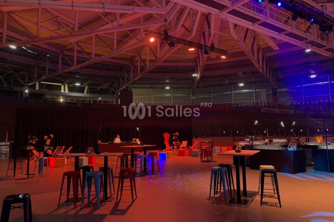 Salle événementielle avec éclairage tamisé, tables hautes et chaises disposées dans un espace ouvert.