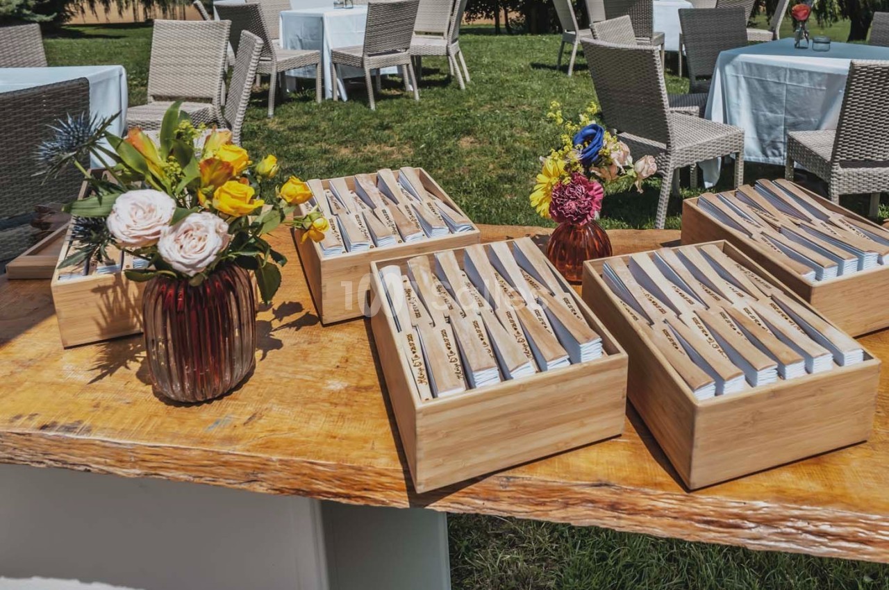 Couverts en bois disposés dans des boîtes sur une table en extérieur, avec des bouquets de fleurs colorées.