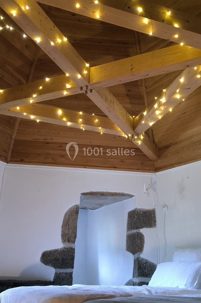 Plafond en bois avec poutres apparentes décorées de guirlandes lumineuses, au-dessus d'un lit avec couvertures.