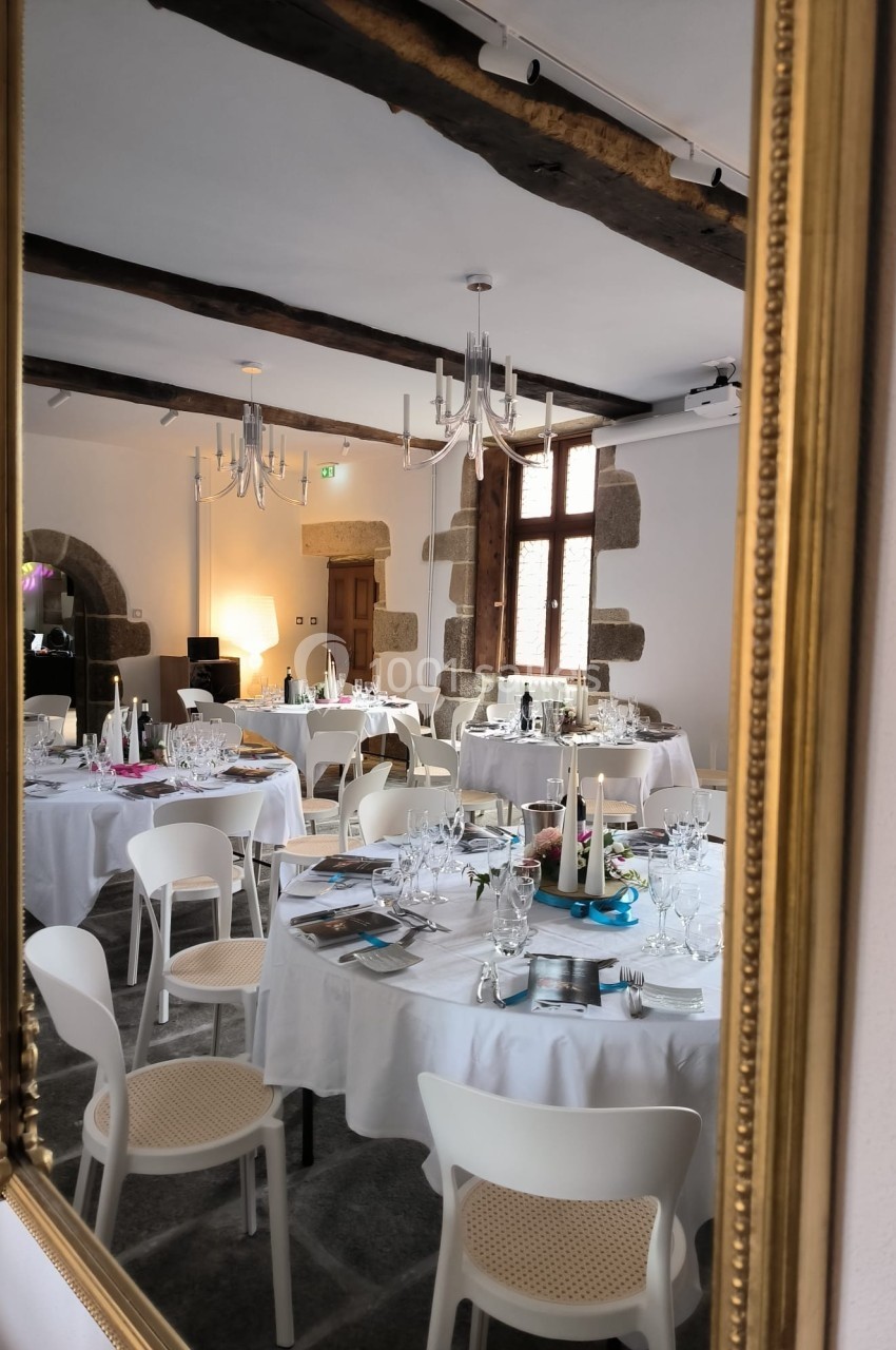 Salle de réception élégante avec tables rondes dressées, vue dans un miroir doré.