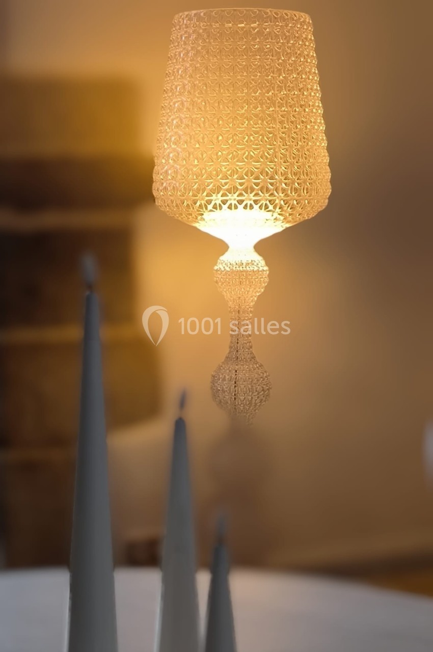Lampe suspendue au design ajouré diffusant une lumière chaude, avec des objets décoratifs en avant-plan flou.