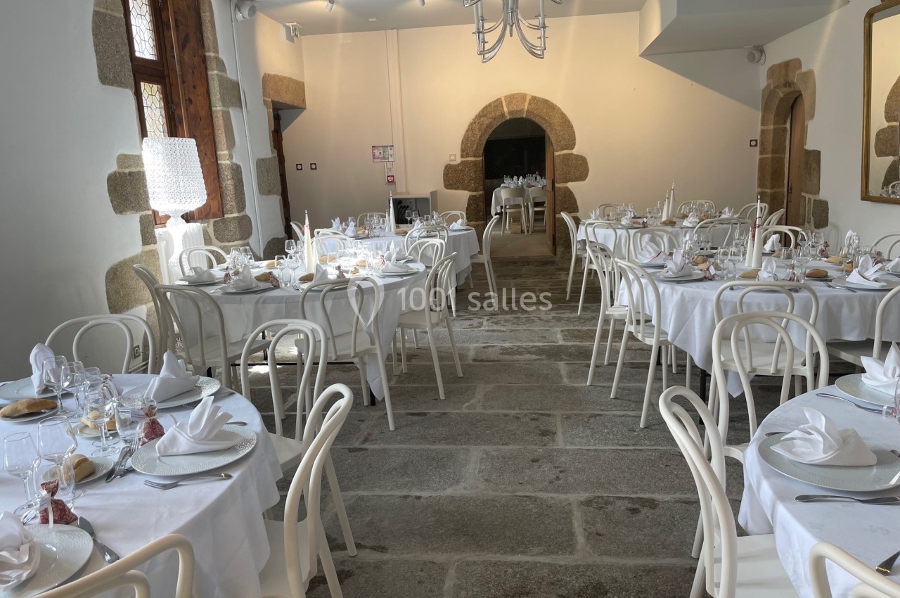 Salle de réception lumineuse avec tables rondes dressées de nappes blanches et chaises en bois clair.