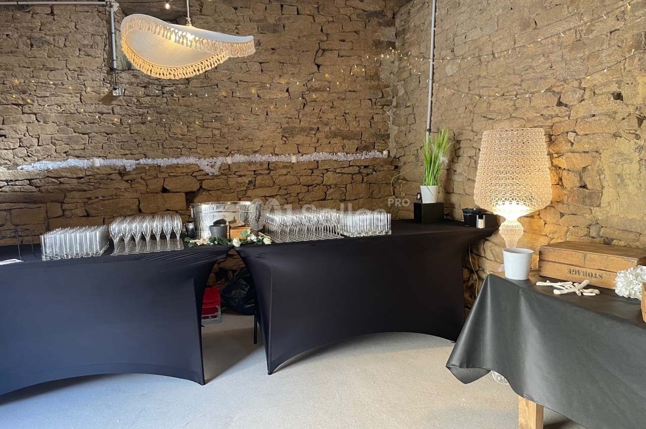 Tables recouvertes de nappes noires avec verres, seaux à champagne et décorations dans une salle en pierre.