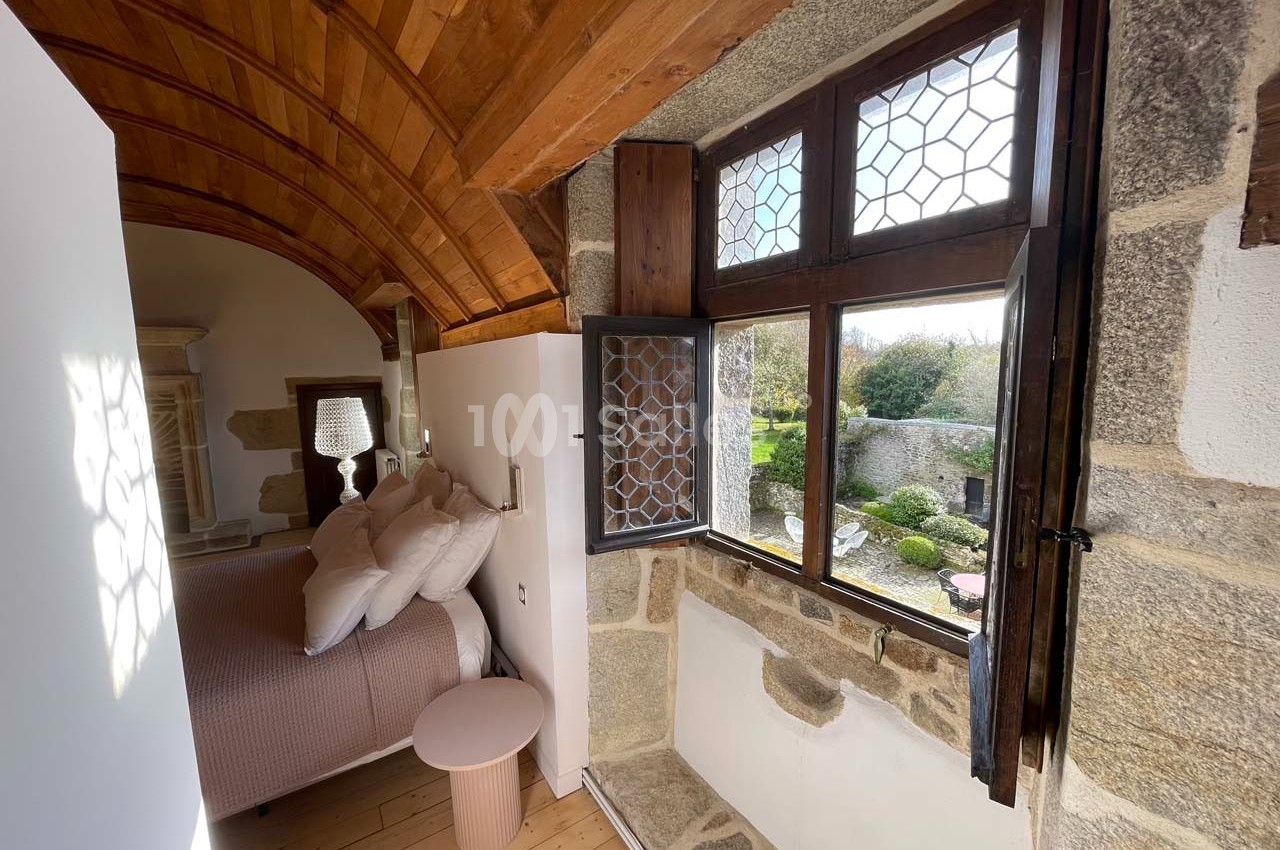 Chambre lumineuse avec plafond voûté en bois, lit double et fenêtre ouverte donnant sur un jardin.