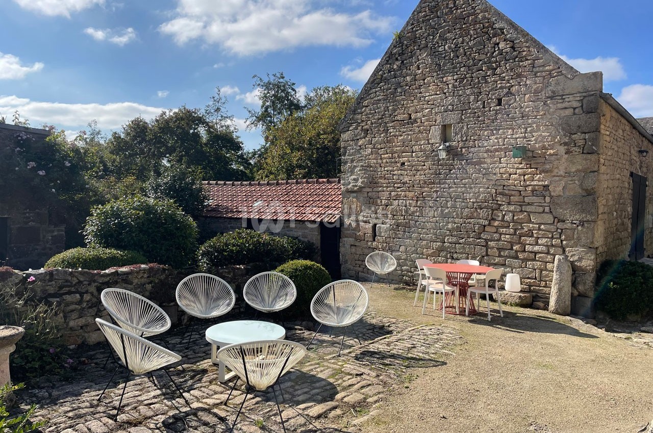 Cour en pierre avec mobilier de jardin moderne, entourée de bâtiments en pierre et végétation sous un ciel dégagé.