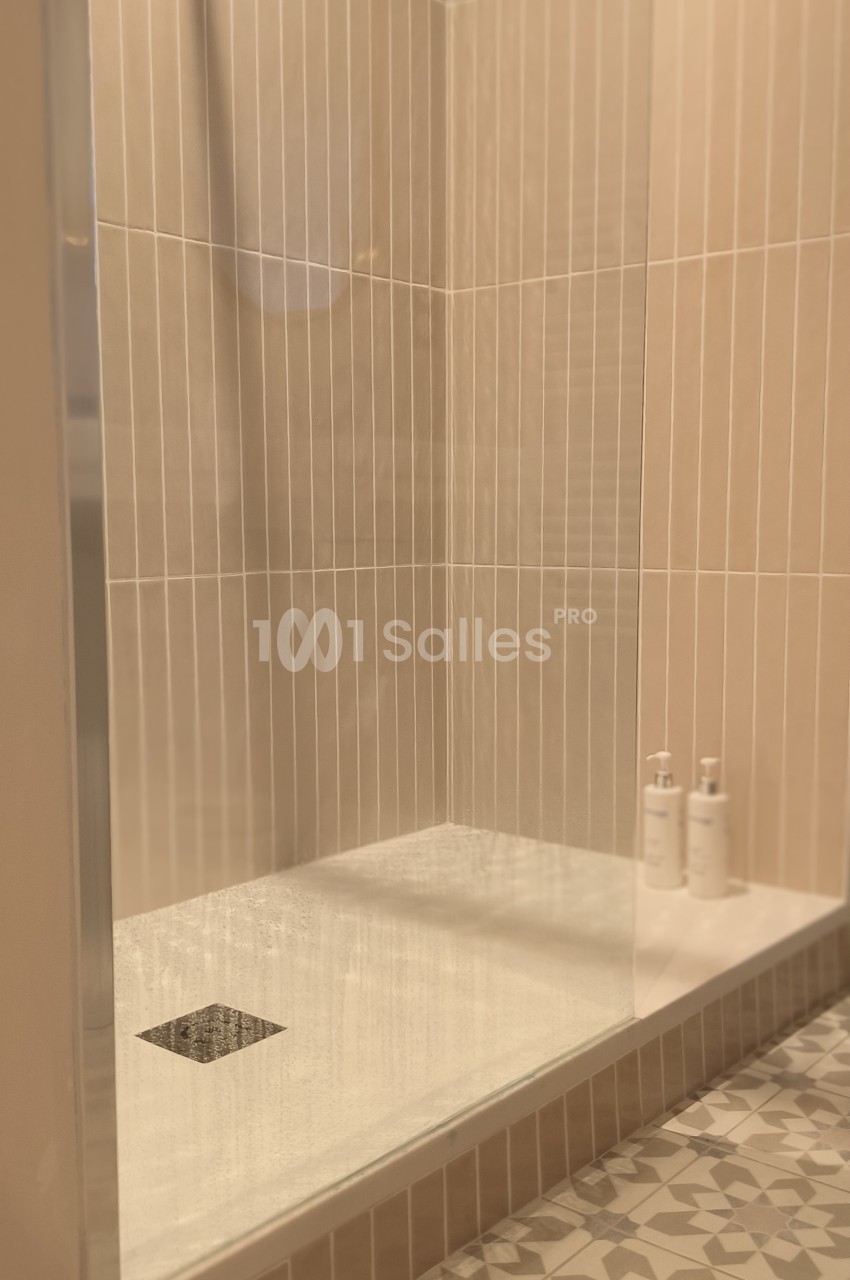 Douche moderne avec parois en verre, carrelage beige vertical et sol à motifs géométriques, deux flacons posés au fond.
