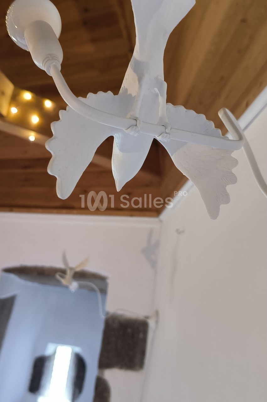 Suspension en forme d'oiseau blanc avec des ailes déployées, accrochée à un plafond en bois dans une pièce lumineuse.