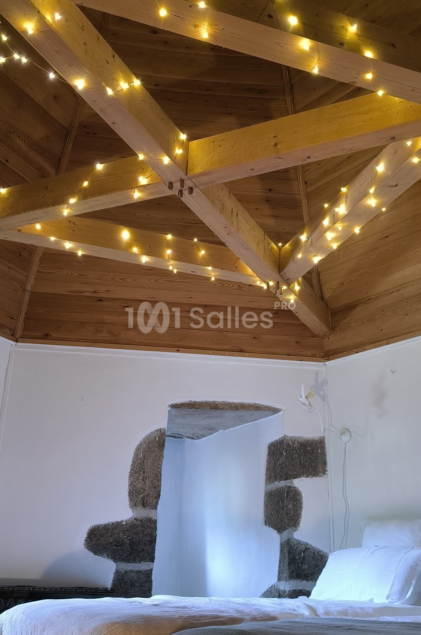 Plafond en bois avec poutres apparentes décorées de guirlandes lumineuses, au-dessus d'un lit avec couvertures.
