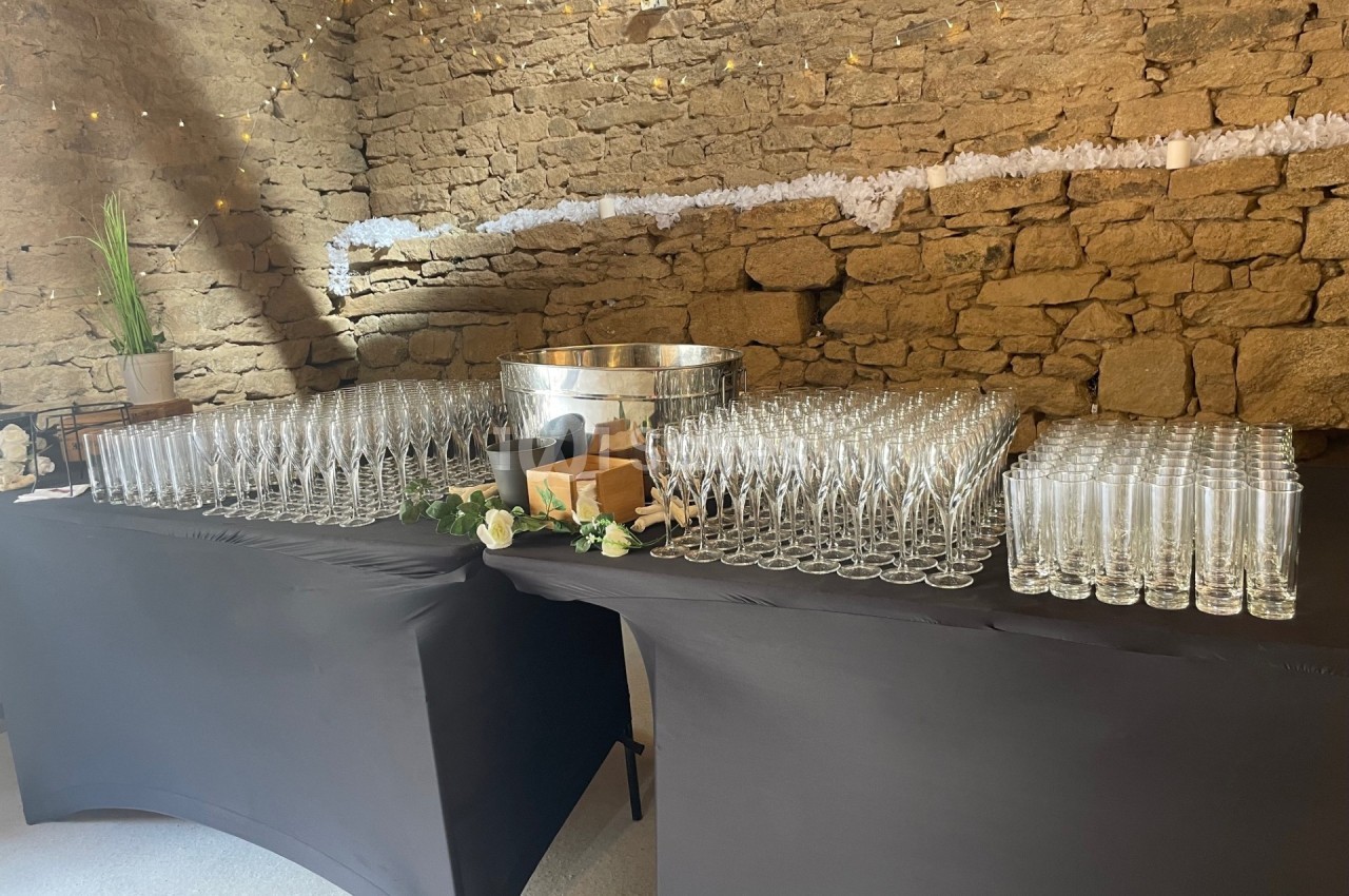 Tables noires dressées avec des rangées de flûtes à champagne et un seau à glace dans une salle en pierre décorée.