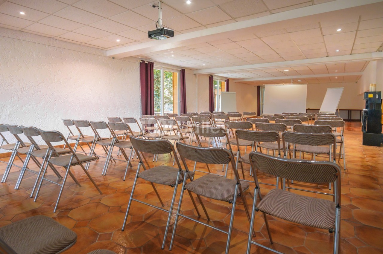 Salle de réunion lumineuse avec chaises pliantes disposées face à un écran de projection et un paperboard.