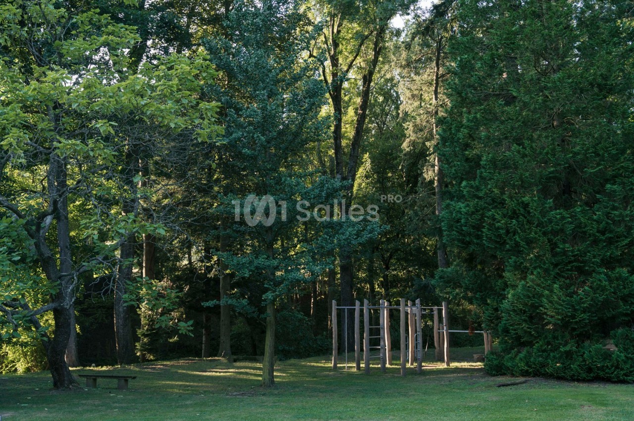 Structure en bois pour jeux d'enfants dans un parc verdoyant entouré d'arbres.
