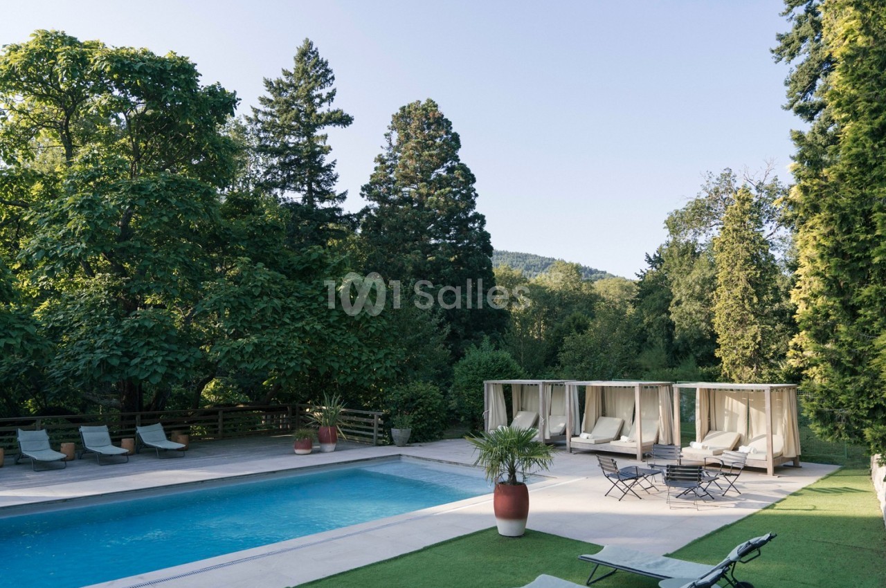 Piscine extérieure entourée de chaises longues, lits baldaquins et végétation luxuriante sous un ciel dégagé.