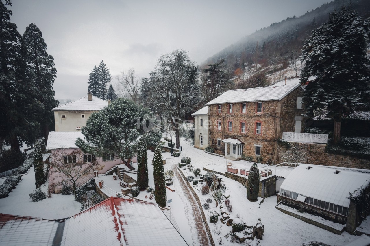 Vue d'un village enneigé avec des maisons en pierre et des toits recouverts de neige, entouré d'arbres et de collines.
