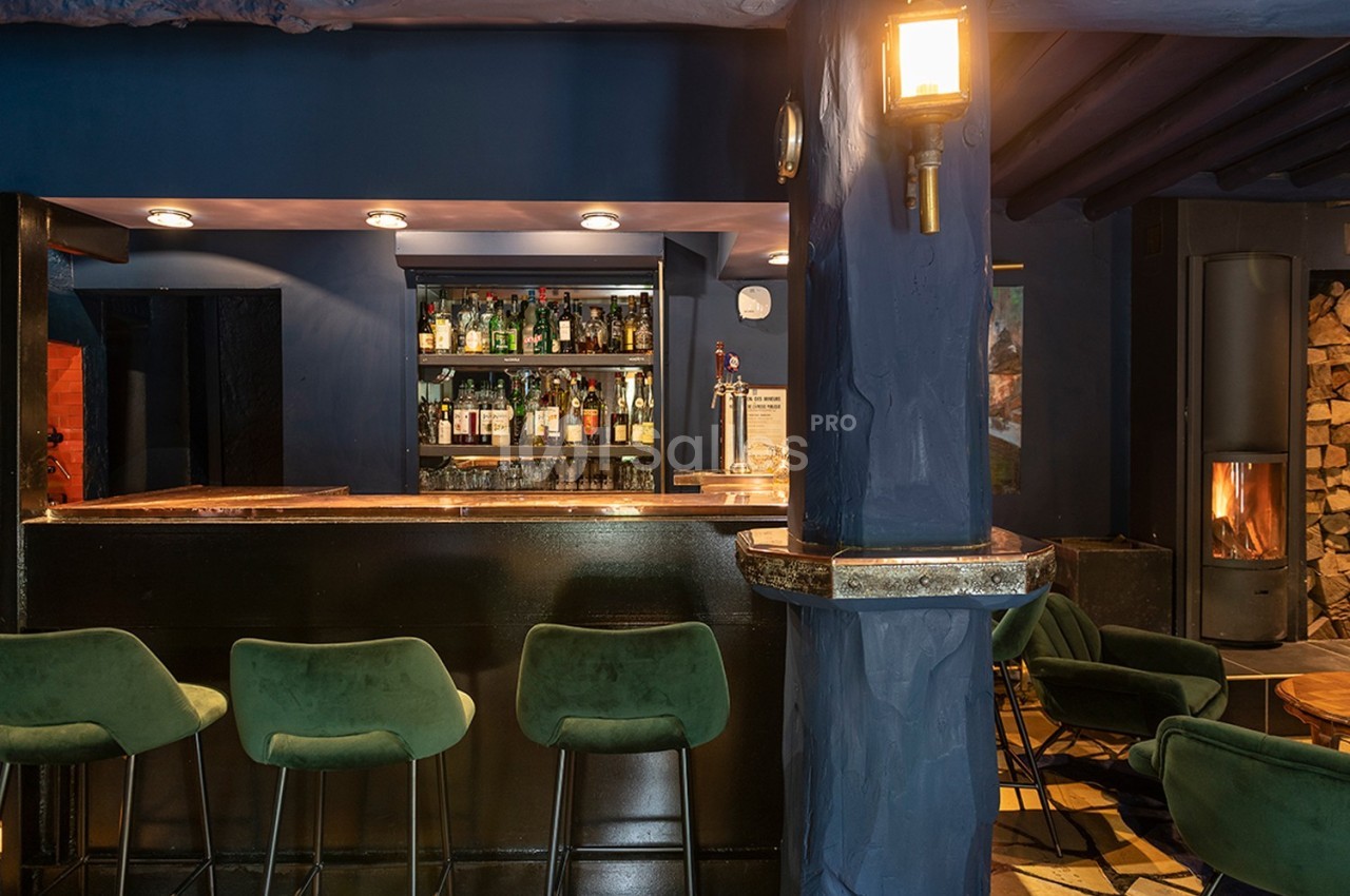 Bar avec comptoir en bois sombre, tabourets verts, étagères de bouteilles et éclairage chaleureux dans une ambiance cosy.
