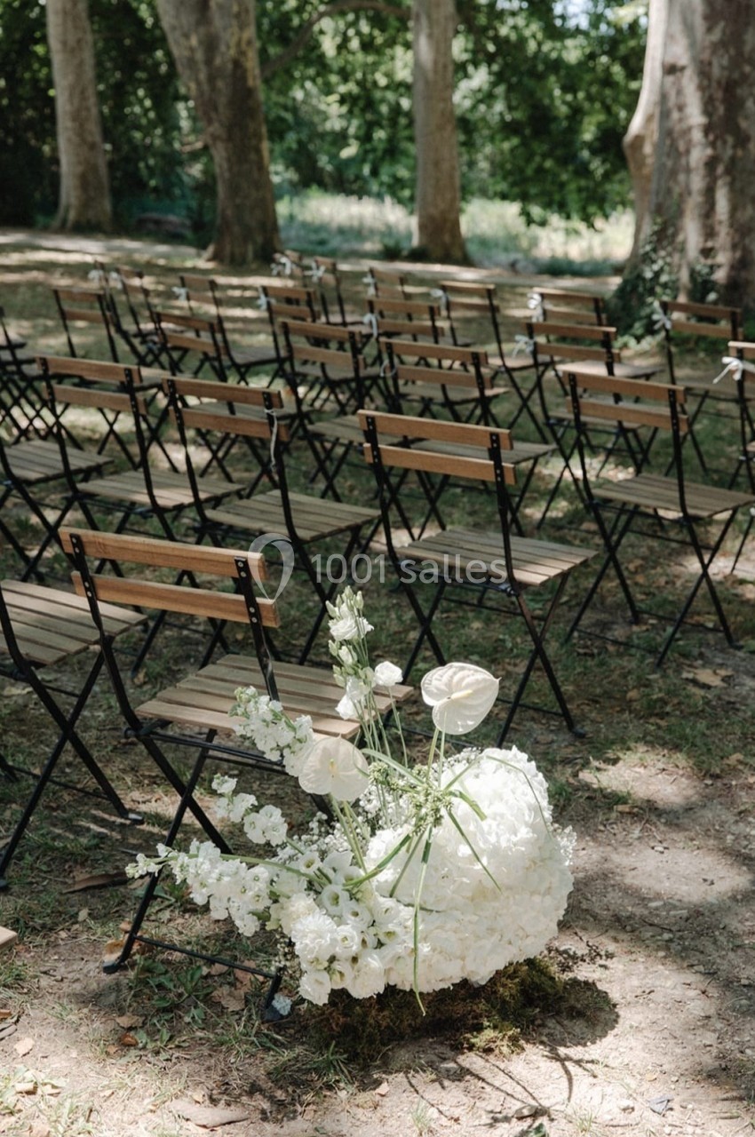 Chaises pliantes alignées en extérieur sous des arbres, avec une composition florale blanche au premier plan.