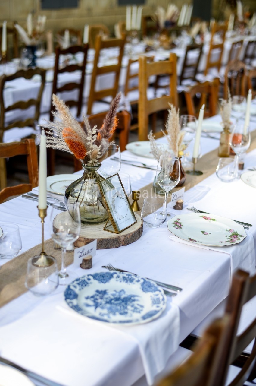 Table dressée avec nappes blanches, vaisselle vintage, chandeliers et décorations florales séchées.