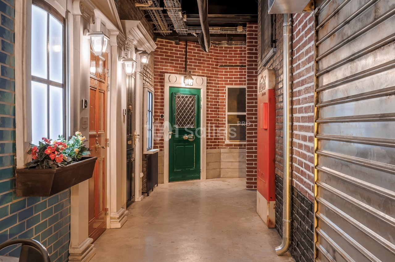 Couloir intérieur avec façades imitant des devantures de maisons, éclairage artificiel et éléments industriels visibles.