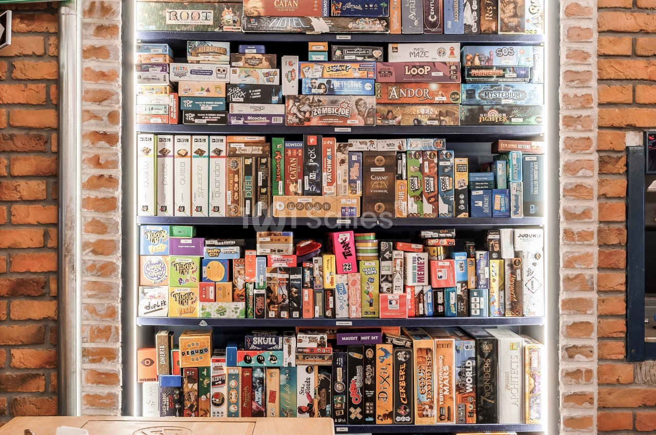 Étagère remplie de jeux de société variés dans un espace intérieur avec murs en briques.