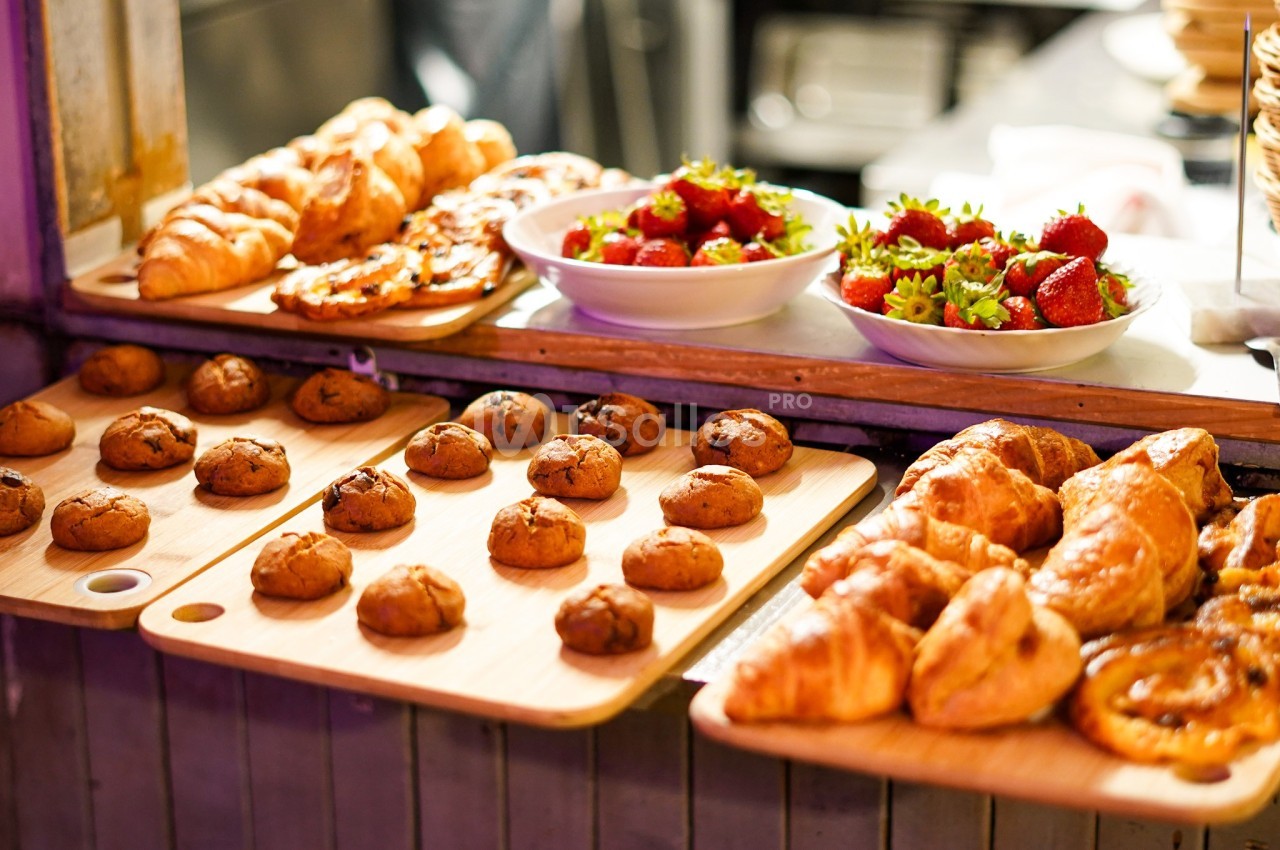 Pâtisseries variées, croissants, biscuits et bols de fraises fraîches disposés sur un comptoir en bois.