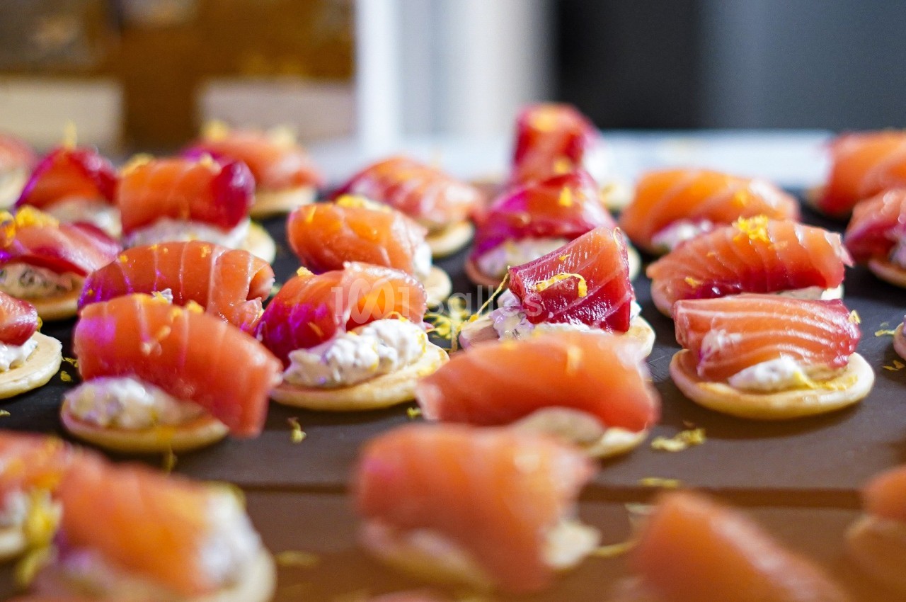 Plateau de canapés garnis de tranches de saumon fumé et de crème sur des blinis, décorés de zestes d'agrumes.