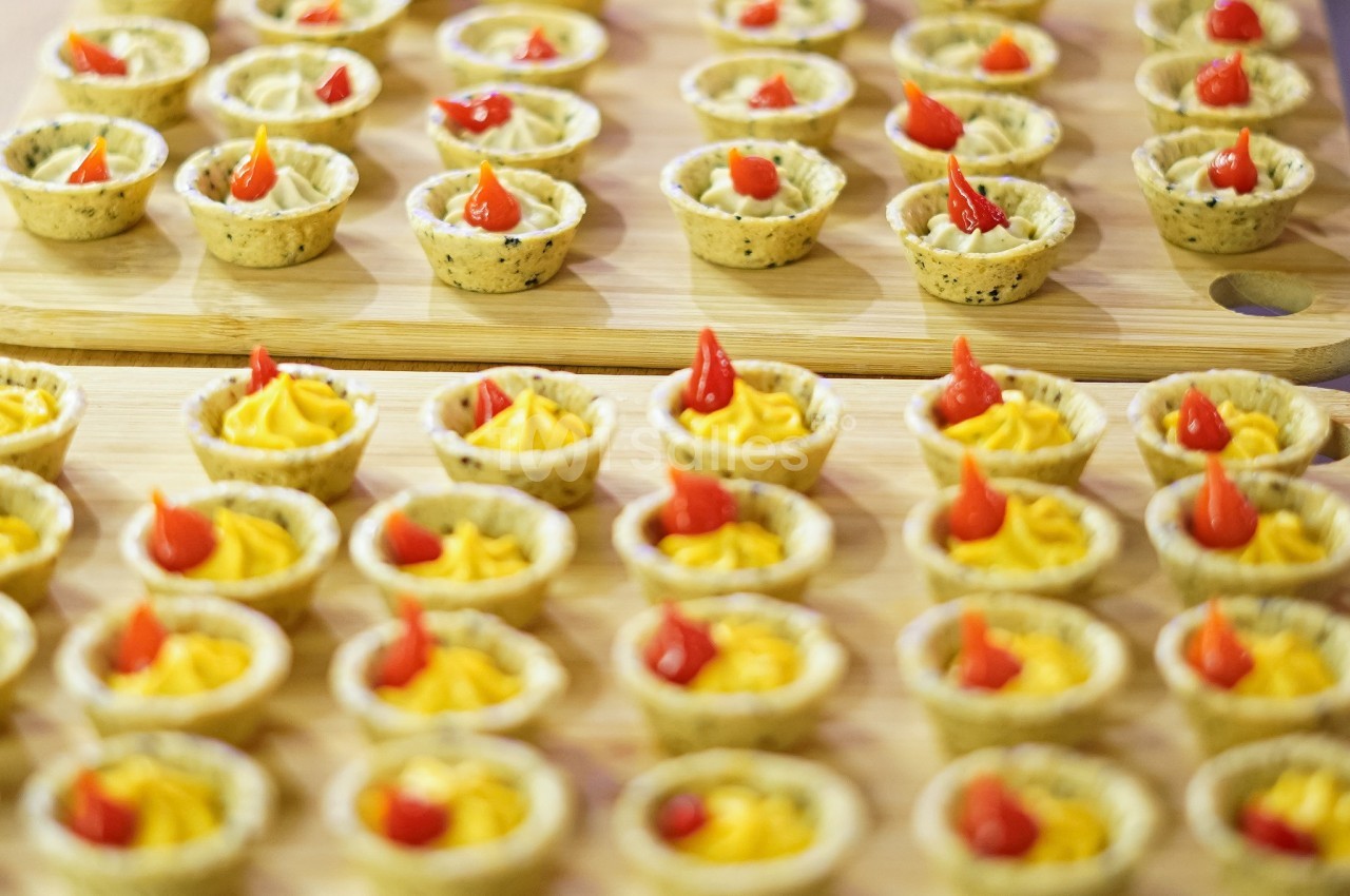Petits amuse-bouches en tartelettes garnies de mousse jaune et décorées de pointes de sauce rouge.