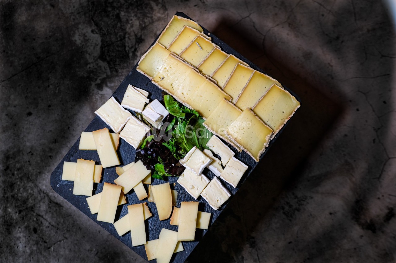 Plateau de fromages variés disposés sur une ardoise avec un mélange de feuilles de salade au centre.