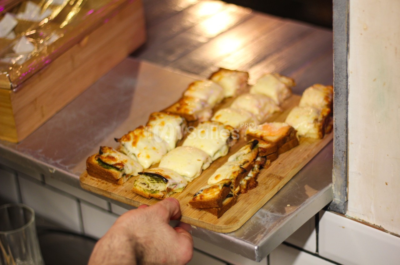 Tranches de pain garnies de fromage fondu et autres ingrédients, servies sur une planche en bois.