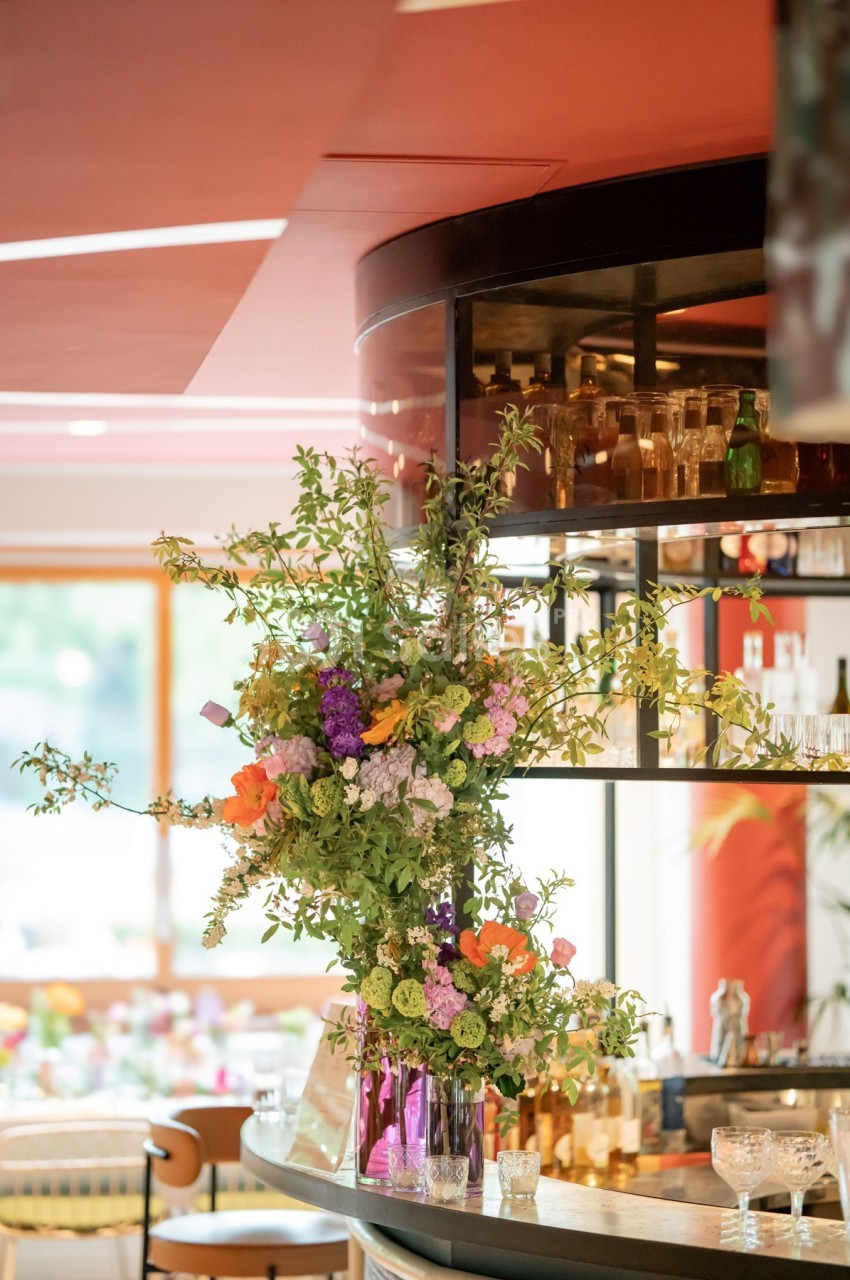 Arrangement floral coloré sur un comptoir de bar moderne avec étagères en verre et lumière naturelle en arrière-plan.
