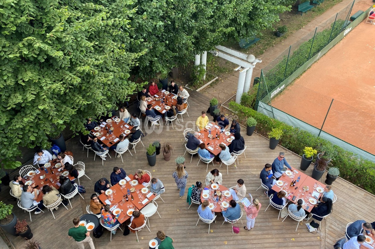 Vue aérienne d'un groupe de personnes partageant un repas en plein air sur une terrasse entourée d'arbres et d'un terrain de…