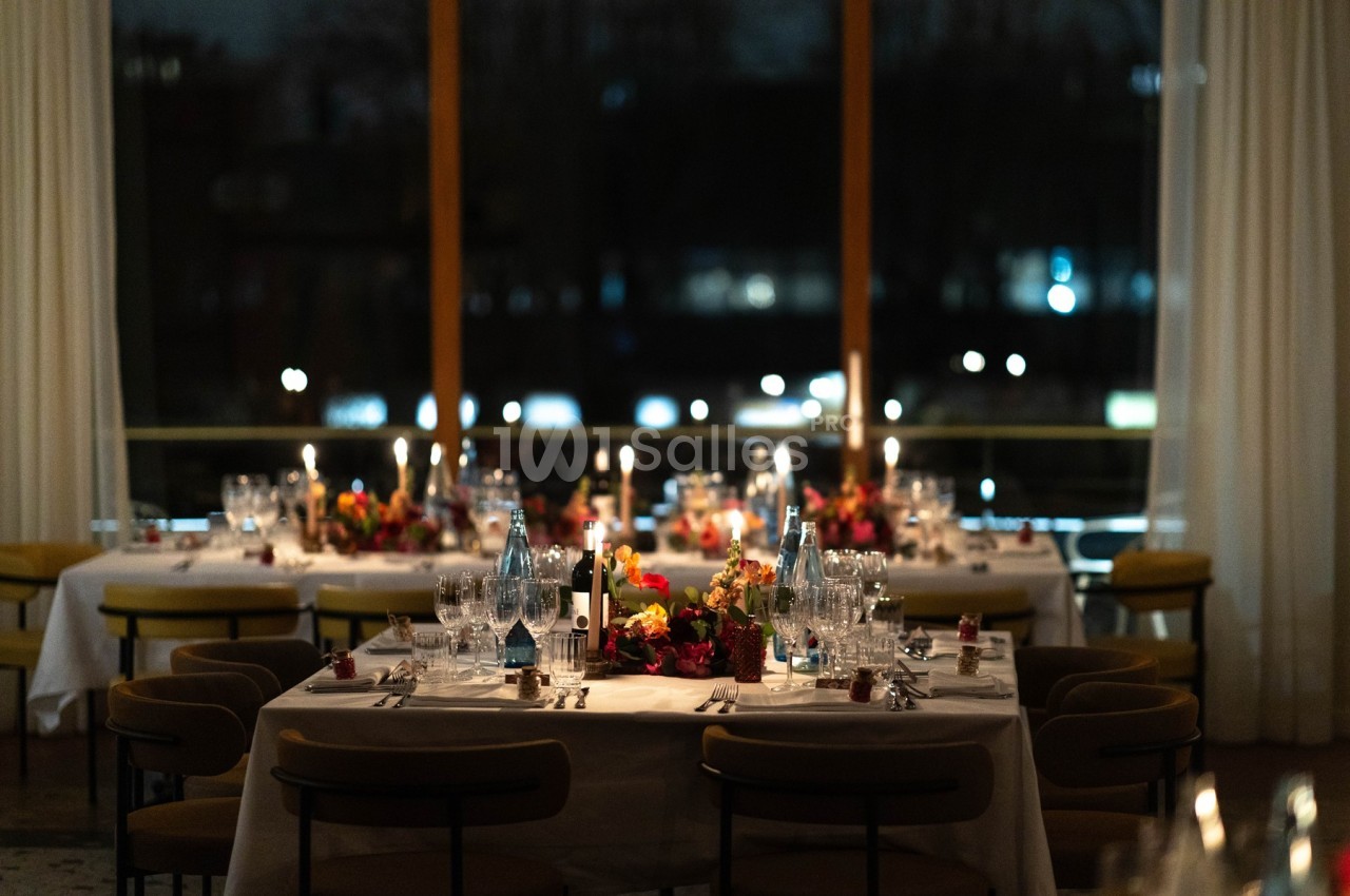 Salle de réception élégamment décorée avec des tables dressées, des bougies allumées et des fleurs colorées.