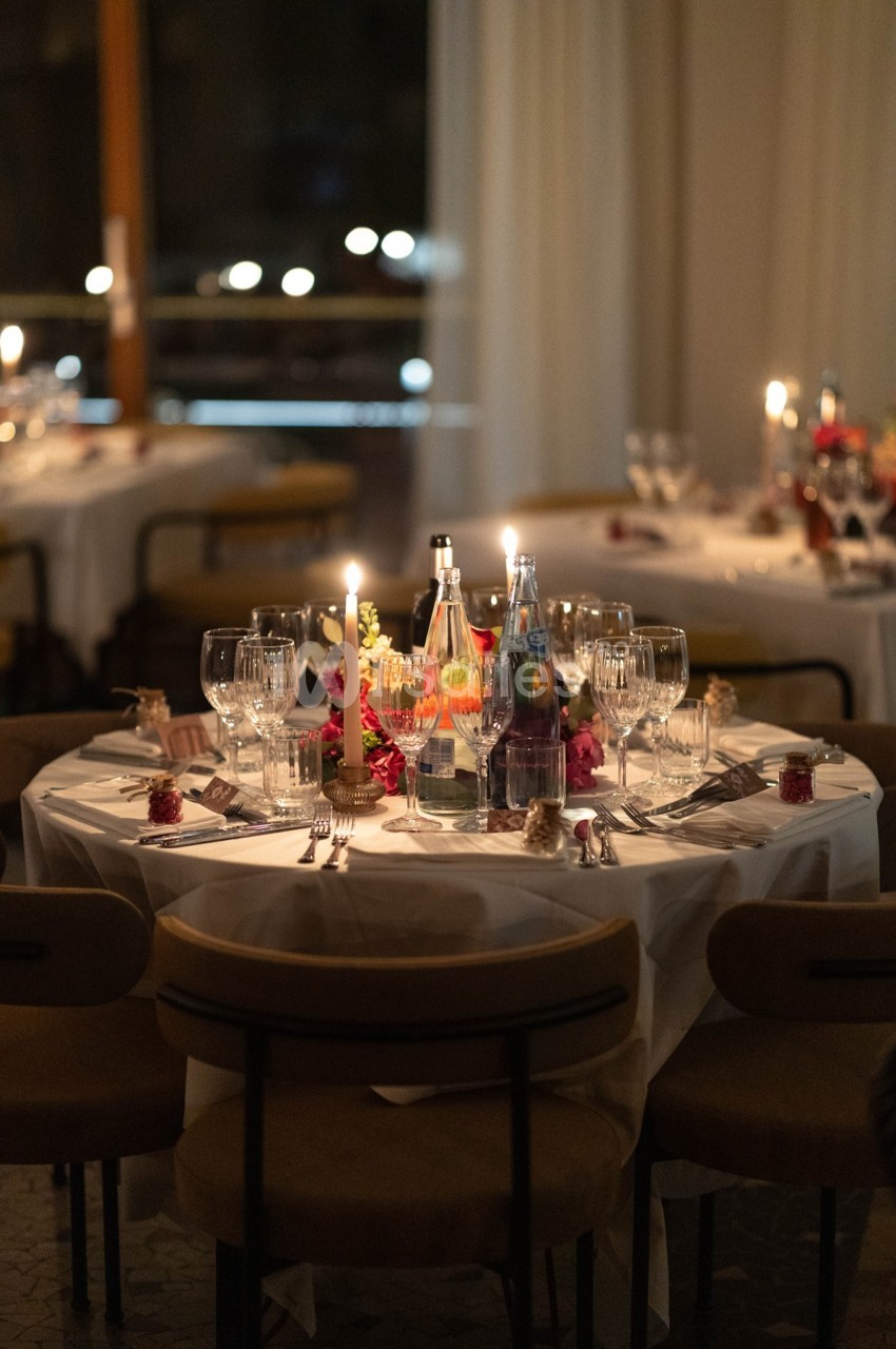 Table élégamment dressée avec nappes blanches, verres, bougies allumées et décorations florales dans une ambiance tamisée.