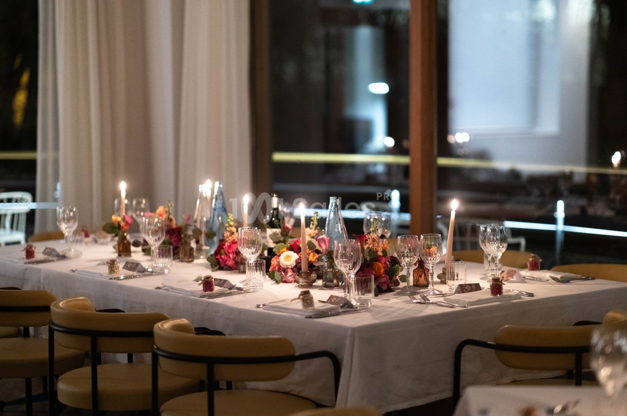 Table élégamment dressée avec nappes blanches, bougies allumées, fleurs colorées et verres en cristal dans une salle…